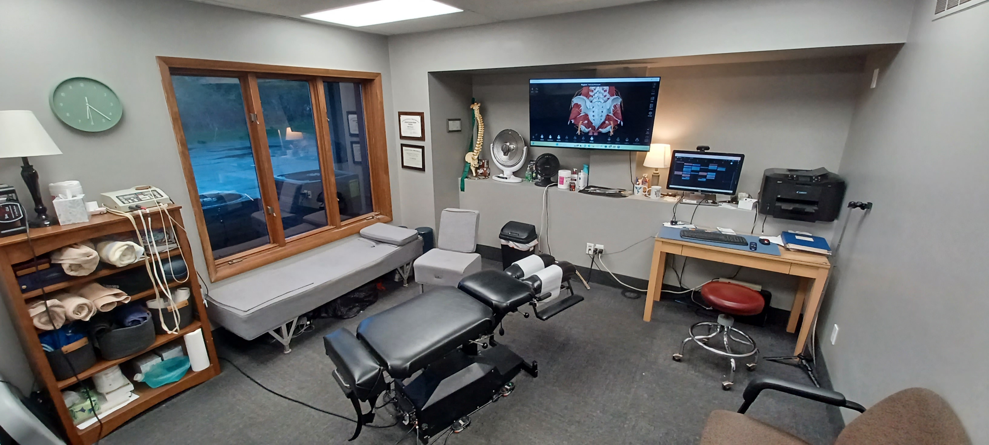 Primary treatment room at Tri-County Chiropractic in Fairport, NY — featuring chiropractic adjusting tables, soft tissue therapy tools, and a large anatomy display screen for patient education